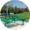 Round image of green picnic table on cement slab in grassy park with trees in the background